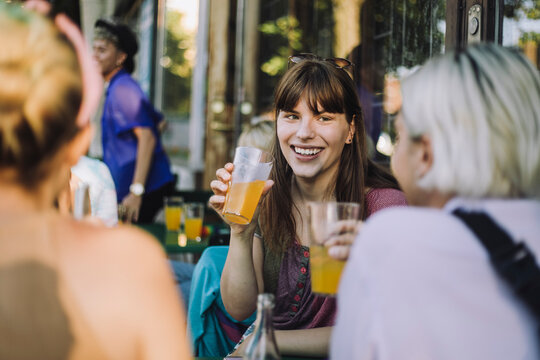 Happy transgender woman talking while enjoying juice with non-binary friends