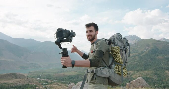 a young happy millennial has a video chat with his followers in picturesque mountains in cloudy weather the blogger shares his impressions of the trip in a vlog Happy hipster enjoying adventure 