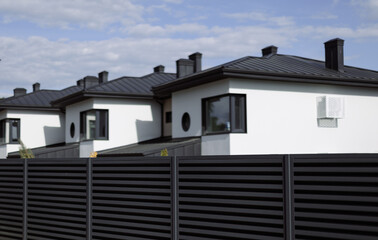 New cottages with a metal black fence on a blue sky background