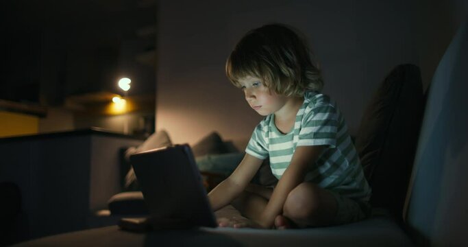 Cute small kid boy in living room using funny editing application on digital computer tablet, enjoying cool video or photo content in social network, playing online games, communicating distantly.