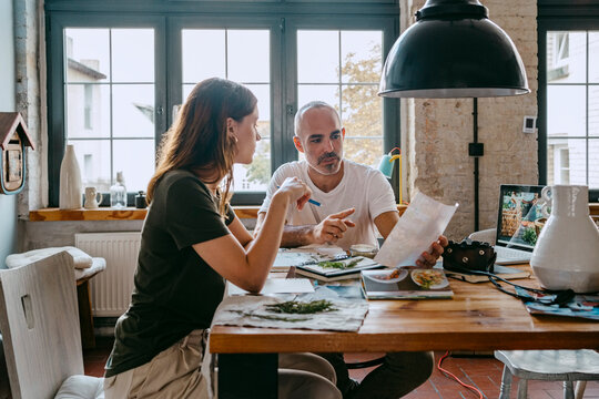 Entrepreneur Explaining Female Colleague While Holding Photograph At Table In Studio