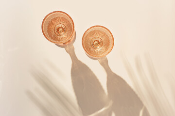 Two wine glasses from pale pink color glass with palm leaf shadows from sun, trendy goblets style...