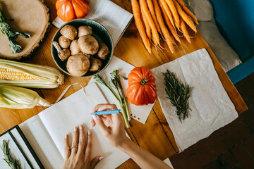 Directly above view of food stylist writing in diary amidst vegetables on table