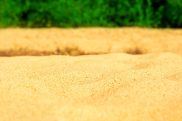 Close-up of clean sand on a river beach with green bushes in the background. City recreation space.