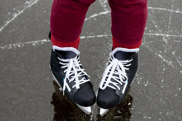 Fototapeta na wymiar Black skates on ice. Women's legs in burgundy pants stand on the surface of a frozen forest lake