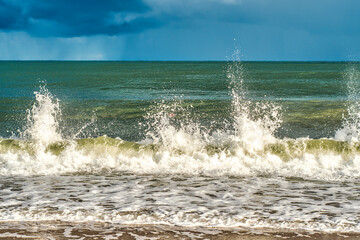 Small sea waves with splashes of water flying up on the coast. A relaxing holiday on the beach. Memories of a summer vacation.