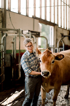 Mature female farmer standing with cow at cattle farm