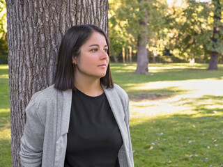 WOMAN IN PARK LEANING ON A TREE