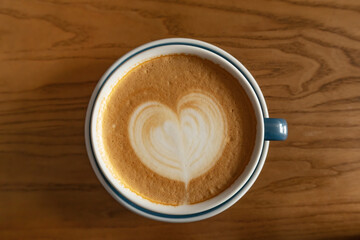 Cappuccino coffee with heart shaped foam in ceramic mug on wooden table top view