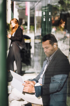Businessman using laptop while sitting at bus stop during sunny day