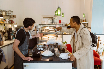 Side view of male cafe owner suggesting food to customer at counter