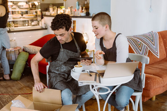 Male and female owners checking box while sitting on chair in cafe