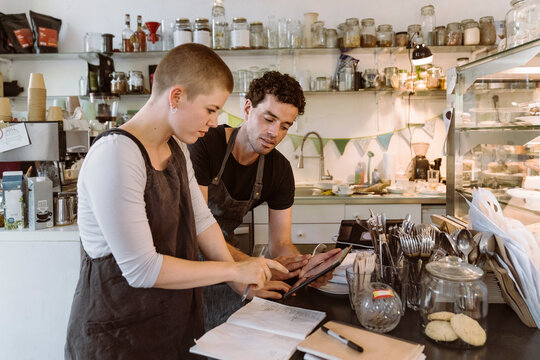 Male and female owners doing inventory using tablet PC at cafe