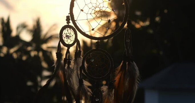 Close up silhouette of dream catcher with feathers flying in wind. Hunter of dreams against sunset. 