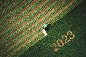 2023 Happy New year concept for agriculture, business, goals, success and new start banner. Industrial tractor on a green field. - obrazy, fototapety, plakaty