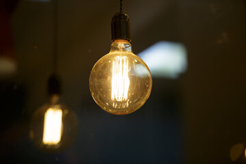 A burning light bulb glows faintly against the background of blurry yellow lights. Energy crisis....