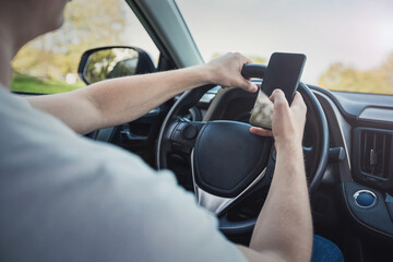 Young driver guy distracted by his phone while in front of the steering wheel, using his smartphone with one hand while driving. Risk and danger situations on the road, violating traffic rules - 551836536