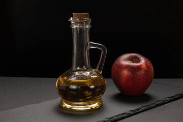 Apple vinegar in glass bottle and fresh red apple on stone board.