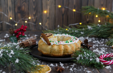 Traditional Christmas cake decorated with white glaze, sprinkles, dried orange slice and fruity apple marshmallows on a wooden snowy background, framed with New Year's details. Selective focus.