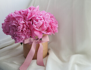 A bouquet of beautiful pink peonies in a box with a bow on a light background