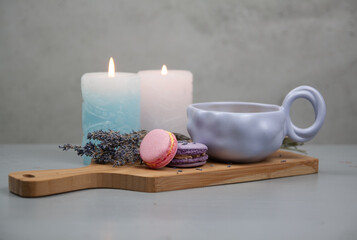 Light purple cup with coffee or milk, dessert macarons next to it, flowers, gray background