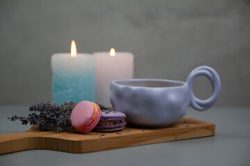 Light purple cup with coffee or milk, dessert macarons next to it, flowers, gray background