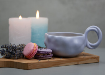 Light purple cup with coffee or milk, dessert macarons next to it, flowers, gray background