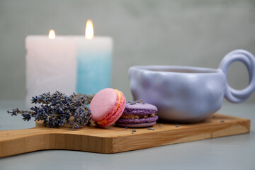 Light purple cup with coffee or milk, dessert macarons next to it, flowers, gray background