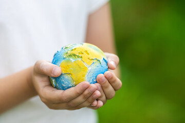 Kid holding small planet in hands against spring or summer green background. Ecology, environment and Earth day concept. 
