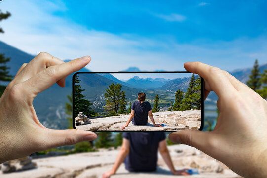 Tourist taking a picture with a mobile phone of a man resting on a rock at the Banff national park.