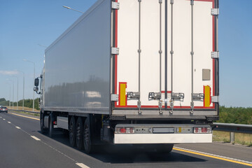 Rear view of white van semi truck drive on suburban asphalted highway road at summer day against blue sky, cargo transportation concept.