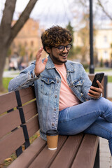Fototapeta premium Indian man is talking on video call with his headphones on his phone while sitting on the bench