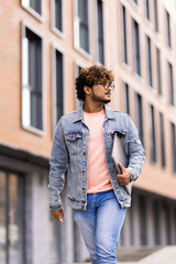 Handsome young indian business man holding his laptop while standing on the street