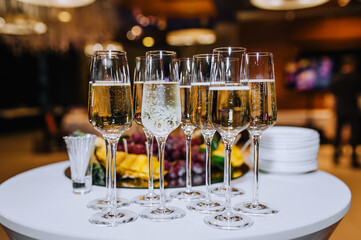 Glass wine glasses with champagne stand on a round white table with fruits and dishes in a restaurant. Photography, banquet, wedding.