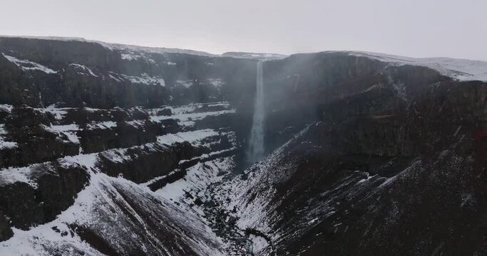 aerial view of hengifoss waterfall during snow with snowflakes moving up