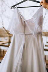 A beautiful long white lace bridesmaid dress hangs on a hanger in the morning outdoors. Photography, wedding, corset back.