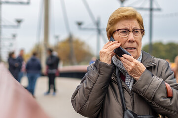 Senior woman talking on the phone in the city, blurred urban background.