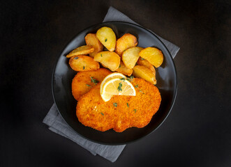 Chicken schnitzel with sauce, fried potatoes and lemon in a plate