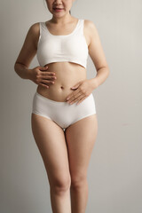 Pretty asian woman wears white lingerie poses against grey background with body care, bra, underwear concept.