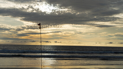 a beach flag pole standing at the beach during the golden dusk 
