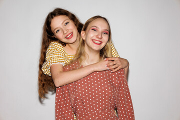 Two young cheerful women hugging on a white background.