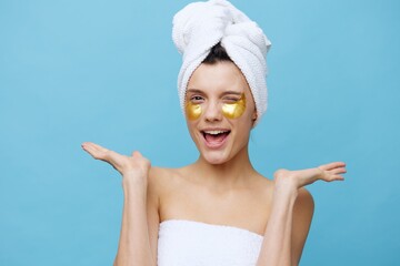  a cute joyful woman with a white smile and clean skin with patches on a blue background with a towel on her head rests and enjoys. Photo for beauty products