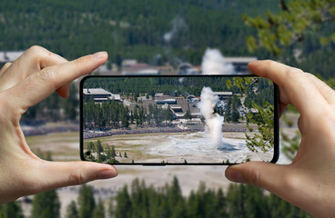 Tourist taking a picture of the erupting geyser old faithful at the Yellowstone national park, USA.