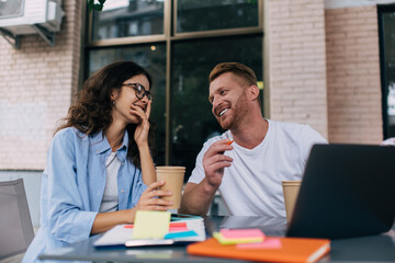 Cheerful young freelancers talking while sitting at table in street