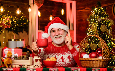 Cozy interior. Christmas eve treats. Winter holiday. Christmas cocoa recipe. Garland lights cozy atmosphere. Cozy home. Hot beverage. Senior man Santa claus drinking tea. New year. Grandpa with mug