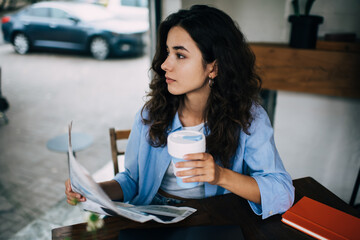 Young woman sitting with cup of coffee and newspaper