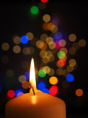 A white candle is burning with colorful Christmas lights bokeh in the background