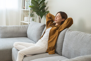 Relaxed serene, happy calm attractive asian young woman peace of mind, relaxing on comfortable sofa, rest in cozy home modern living room, breathing fresh air and eyes closed, dreaming enjoy wellbeing