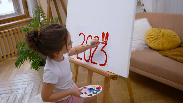 A girl draws 2023 with red bunny ears. Symbol of happy Chinese 2023 New Year.