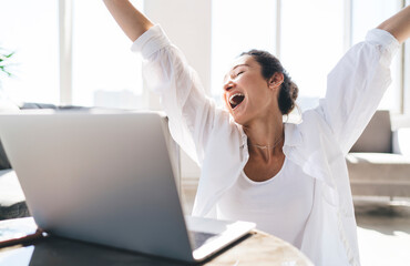 Happy woman with laptop raising arms in victory gesture